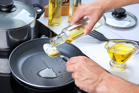 男人从瓶食用油涌入勺子在煎锅图片