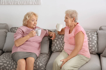 在家坐在沙发上喝咖啡的老年妇女