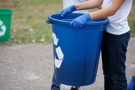 s hands holding a dark blue recycling container. Child collectin