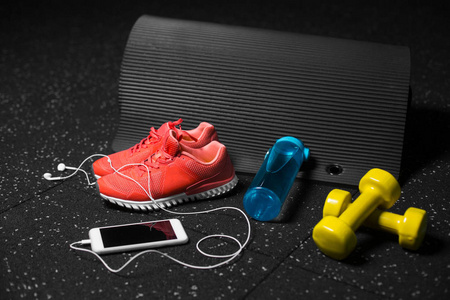 小黄色哑铃垫蓝色瓶子，装满水，明亮的粉红色运动鞋和现代白色智能手机与手机在黑色背景。 运动和训练理念。 复制空间。
