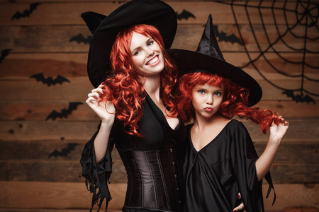 万圣节的概念   美丽的白人母亲和她的女儿在巫婆装束庆祝万圣节假扮与蝙蝠和蜘蛛网木制演播室背景上的长长的红头发