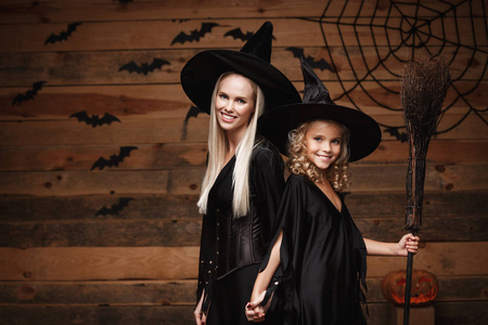 万圣节的概念   开朗的妈妈和她的女儿在巫婆装束庆祝万圣节蝙蝠和蜘蛛网木制演播室背景与弯曲南瓜合影