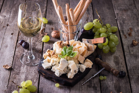 不同种类的奶酪 葡萄酒 水果和零食仿古木制的桌子上。静物的概念