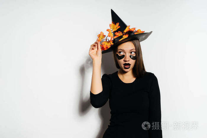 时尚漂亮的女巫看起来到一边和持有他顶大帽子秋天叶子万圣节风格万圣