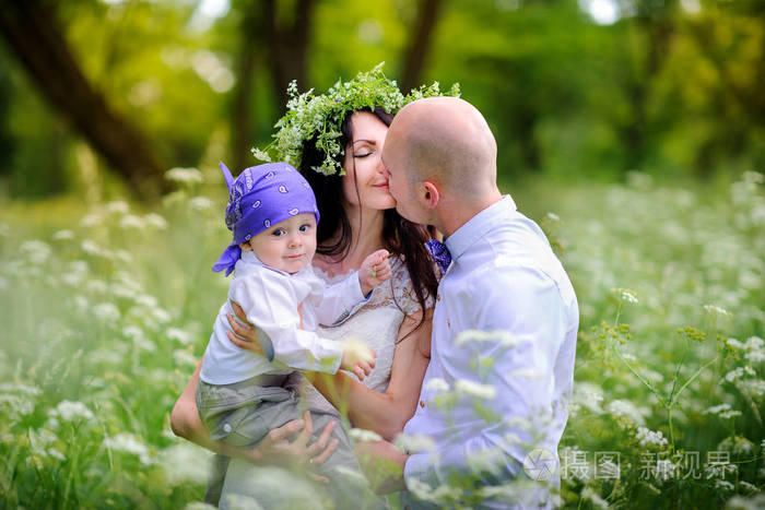 年轻的一家人和孩子们在美丽的公园里散步,在夕阳下,友好地拥抱和亲吻