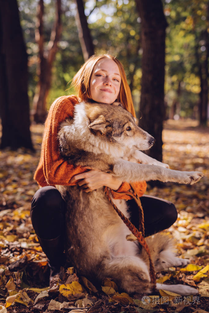一个可爱的女孩拥抱她的狗和直接面对镜头飘零的落叶温暖的秋日
