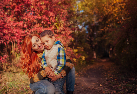 幸福的母亲和她的小儿子走和乐趣在秋天的树林