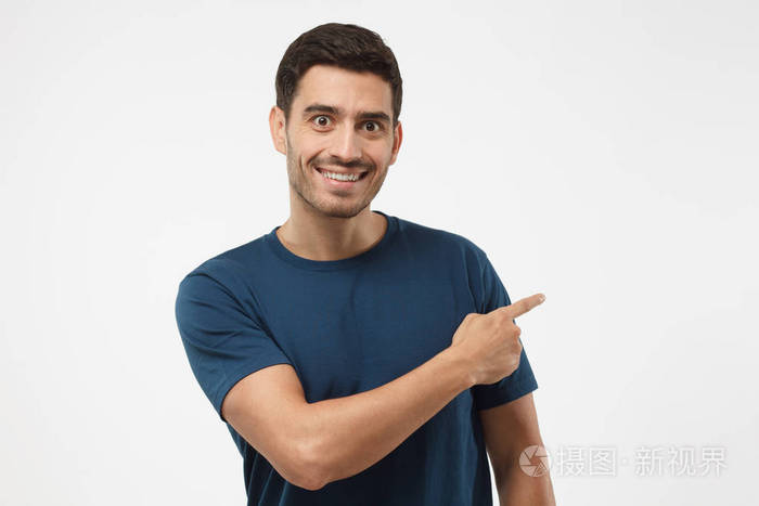 时髦的欧洲人在蓝色的tshirt指着他的手指在灰色背景上的孤立