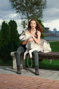 女孩坐在一起在城市公园的赫斯基狗。在一条长凳上的狗