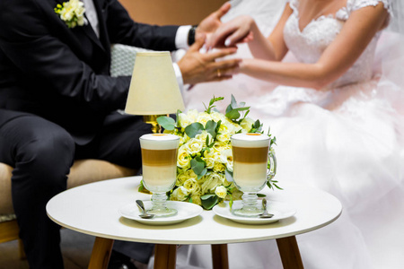 手中的新娘和新郎为一杯咖啡。在桌子上的婚礼花束
