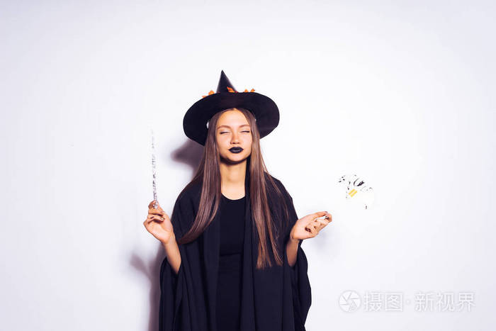万圣节女巫用魔法棒美丽年轻惊讶的女人巫婆帽子和服装宽的万圣节晚会