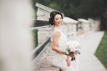 美丽的新娘在优雅的白色连衣裙，抱着花束摆在公园里