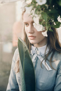 年轻漂亮严重的女孩，一头棕色的长发，穿着浅灰色的裙子在复古的风格，造成附近温室满植物白花的肖像