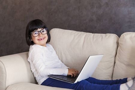 微笑的小女孩戴着眼镜使用她的笔记本电脑