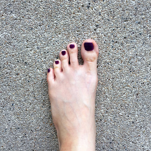 美丽的指甲，关闭了女人的的双脚和红色指甲油上水泥地板背景