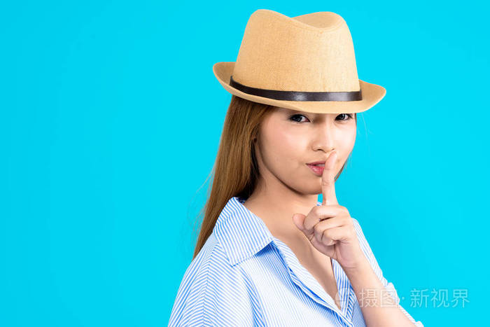 年轻的亚裔女子和孤立在蓝色背景上的秘密嘘姿势