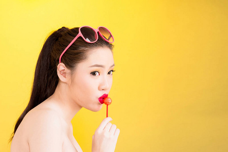 年轻的亚裔女子亲吻棒棒糖隔离在黄色背景上