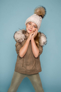 可爱的小女孩穿着冬天的衣服，站在蓝色背景上的皮毛帽子和冬季夹克
