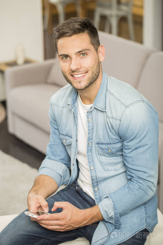 使用智能手机坐在沙发上的英俊男人微笑着