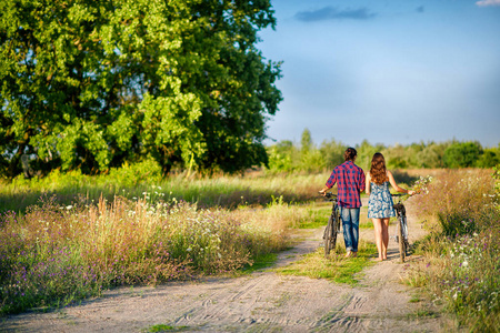 年轻的幸福夫妇骑着自行车在傍晚的田野里散步照片