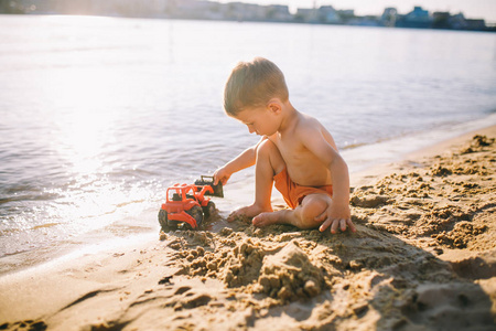 河玩具红色拖拉机附近的沙滩上玩耍的孩子男孩