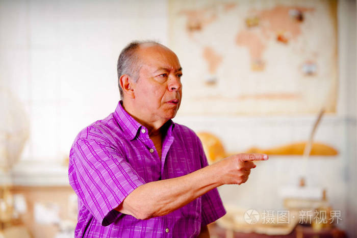 愤怒的老人,用手指向某个地方在一个模糊的背景穿紫色方形 t 恤的肖像