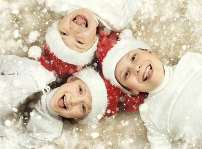 幸福的孩子在一起躺在木制的背景下，身着圣诞圣诞老人的帽子有乐趣，冬天假日概念 雪装饰，黄定调子