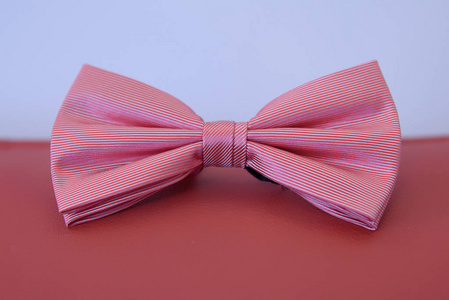 柔滑的条纹图案定位在模糊背景的红色皮革垫上粉红色蝴蝶结领带