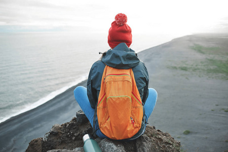 女人徒步旅行者站在一座山的顶上和享受日落在冰岛的背包