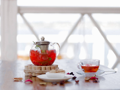 一个透明的茶壶，里面装满了草莓茶，在餐馆的木桌上放着红色的醋栗。 一种浆果红色饮料，背景模糊，带有香料。 有机饮料。