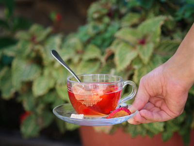 s hand is holding a small cup on a saucer full of fruits tea on 