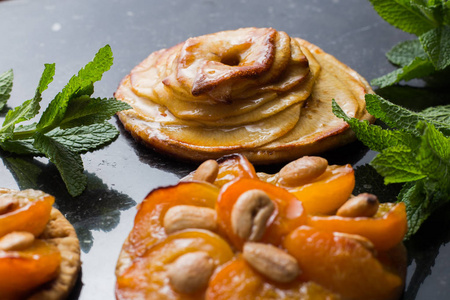 与杏桃和苹果的酸。传统的法国馅饼加黑大理石背景上的水果。装饰的杏仁和薄荷叶子。美味甜点与副本空间特写