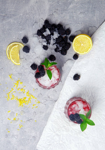 在冰冻的白色背景上，可以看到两杯冰饮料和薄荷和黑莓的组成。成熟，新鲜的黑莓和一个切黄柠檬为一个不含酒精的冰沙。
