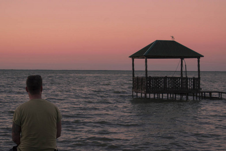 日落时, 男子坐在湖边, 看着水面上的房子