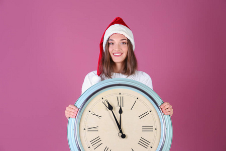 在圣诞老人的帽子，带有时钟的颜色背景的年轻女人。圣诞倒计时概念