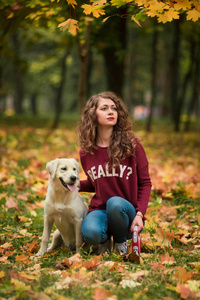 卷发女人和她的狗坐在秋天树叶在户外