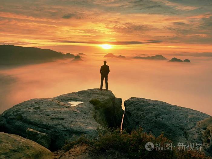 男子站独自在岩石的山峰上.望着秋天太阳在地平线上的徒步旅行者.