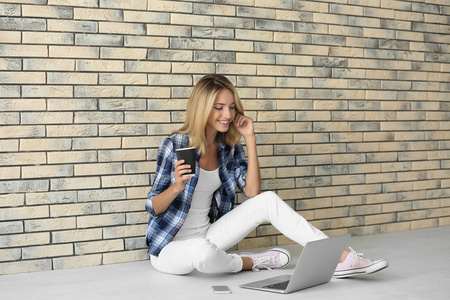 漂亮女人与现代笔记本电脑坐在靠近墙面砖