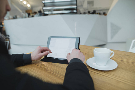 一个男人在网吧里用平板电脑坐在咖啡馆里喝一杯咖啡。学生在明亮的时髦的咖啡馆里使用平板电脑