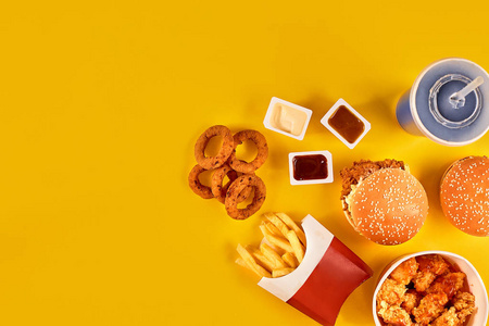 快餐菜顶视图。法式炸薯条，汉堡，沙拉酱和番茄酱的酱汁，在黄色背景上
