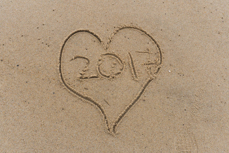 心脏和年2017画在沙滩上的沙子。沿着海洋海岸的浪漫象征, 水波将冲走大海。永远爱的标志