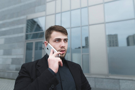 在一座现代建筑的衬托下, 一个美丽的男人带着胡子在电话里交流的街道肖像。商业肖像。看远