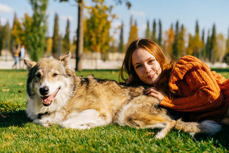 一个穿着橙色的毛衣的女孩在公园里的草坪上在于她的狗。温暖的秋日