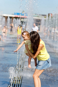 母亲和孩子在炎热的夏天一天玩水射流的喷泉