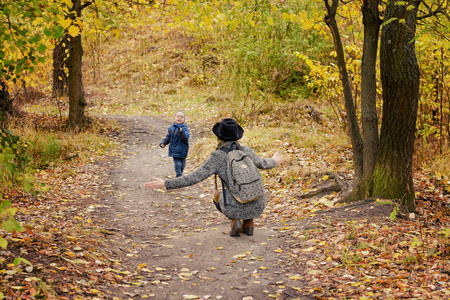 男孩跑去见她妈妈。秋天的公园。后视图