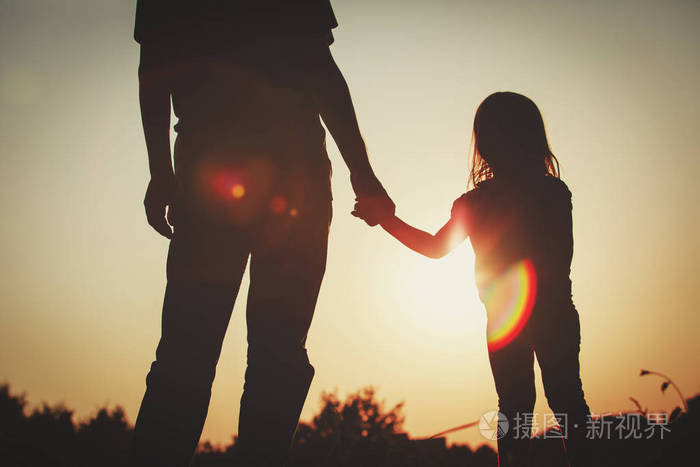 小女孩牵着父的手在日落时的剪影