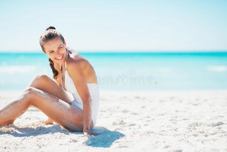 微笑的年轻女子坐在沙滩上看着复制空间
