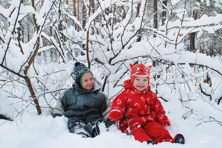 冬天的男孩和女孩坐在雪地里的灌木丛里