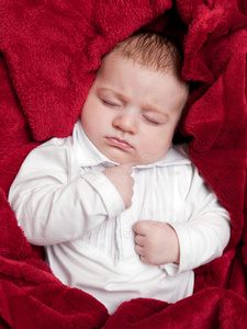 可爱的3个月大的婴儿，睡在铺着红毯子的床上