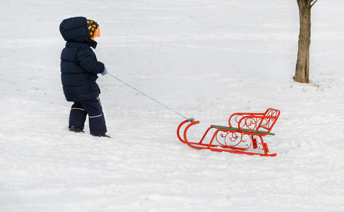 小男孩拉着雪橇穿过冬天的雪图片